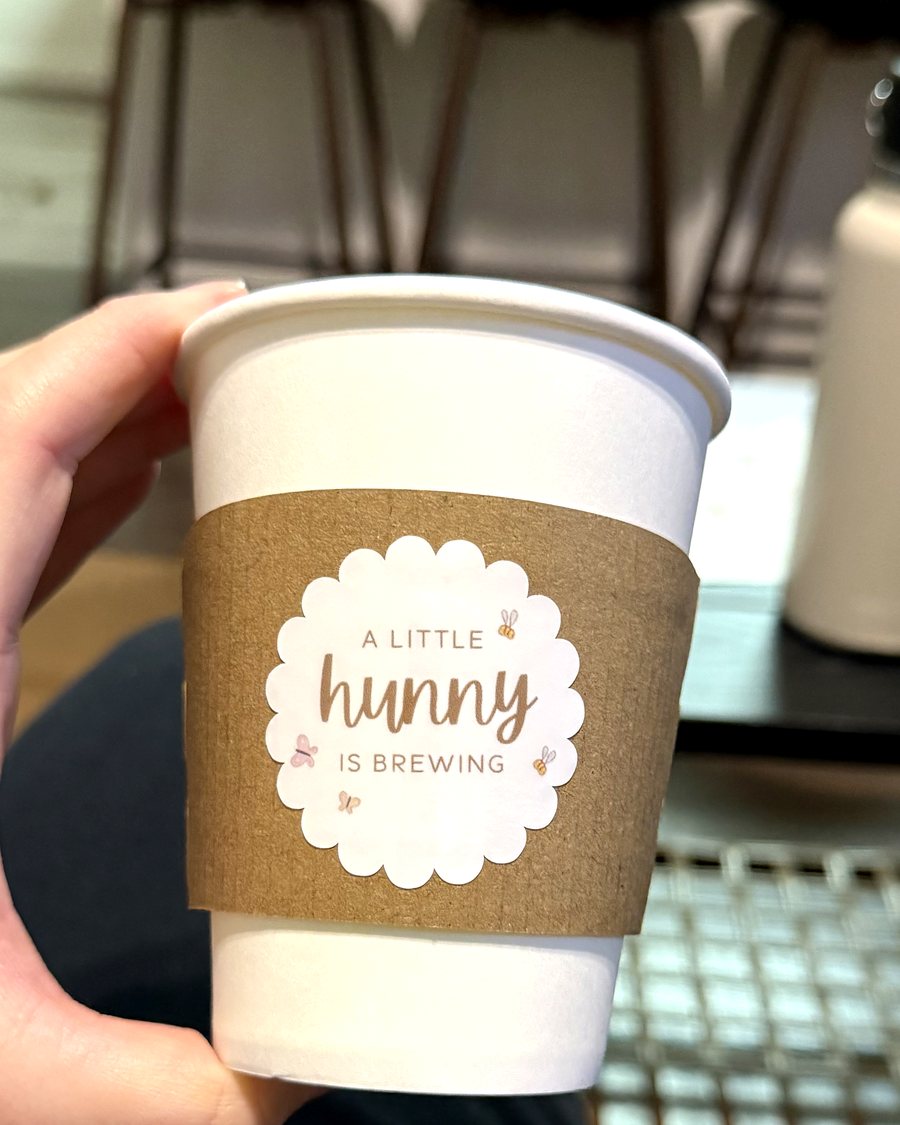 Coffee cup with kraft sleeve and scalloped label reading a little hunny is brewing