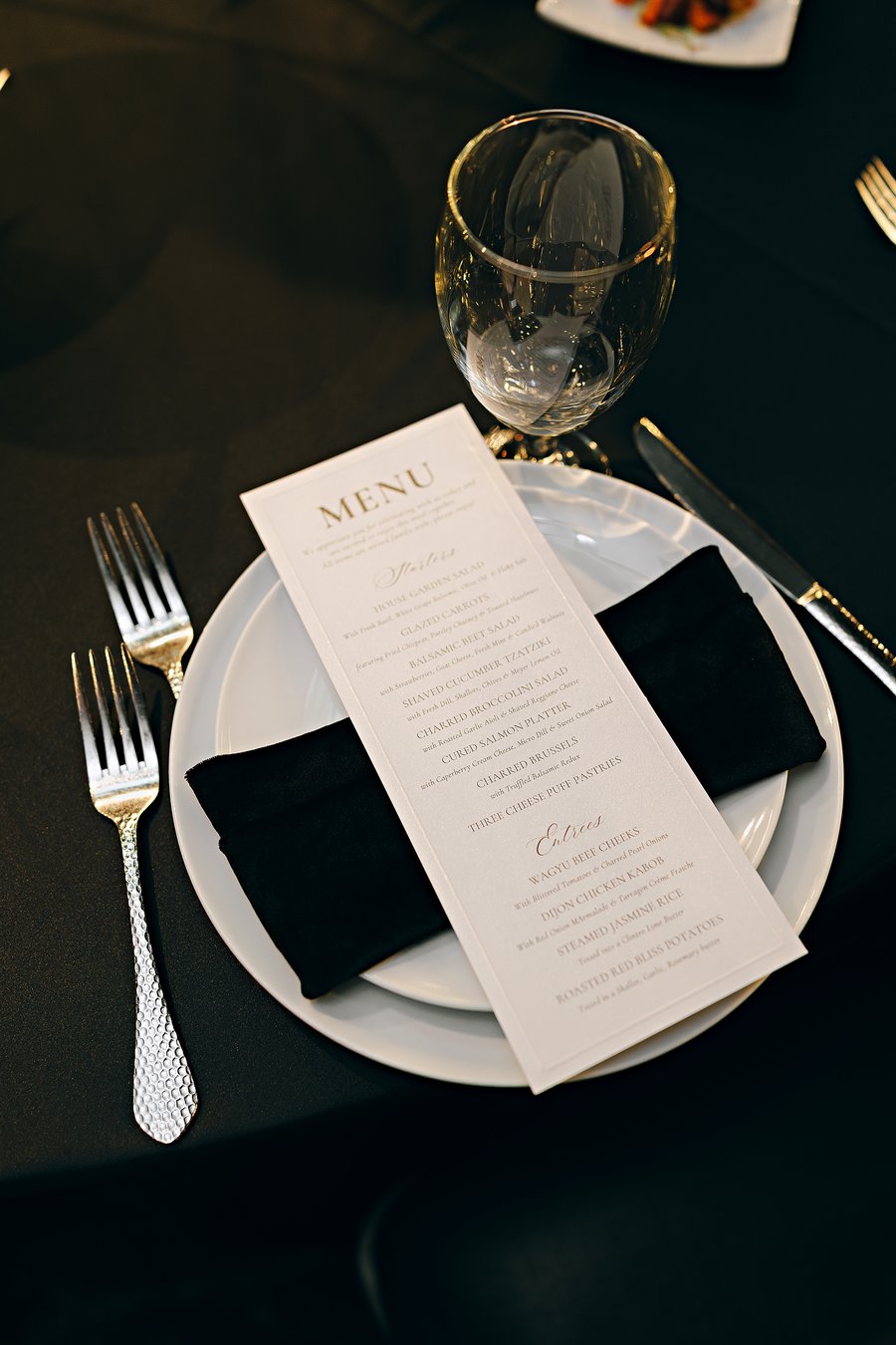 Embossed wedding dinner menu in gold script on a black tablescape